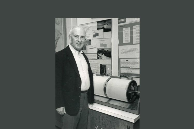 A black and white photo of Lynn Sykes standing by a round machine