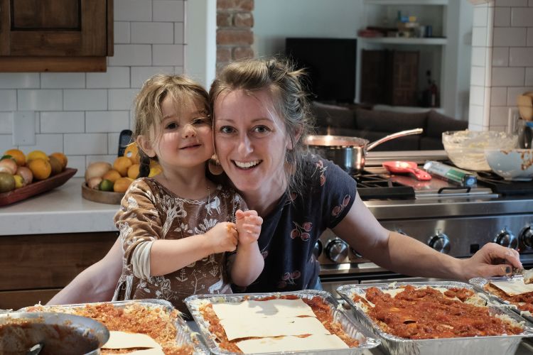 A photo of MIT alum Rhiannon Menn (right) and her daughter (left) leaned over trays of lasagna in a kitchen