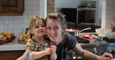 A photo of MIT alum Rhiannon Menn (right) and her daughter (left) leaned over trays of lasagna in a kitchen